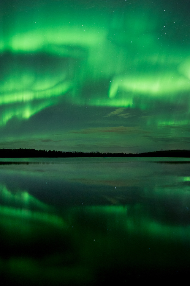 Зеленое северное сияние отражается в воде озера ночью 