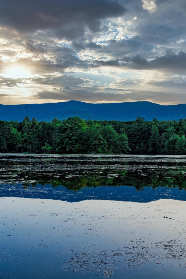 Солнце пробивается сквозь облака в небе над озером