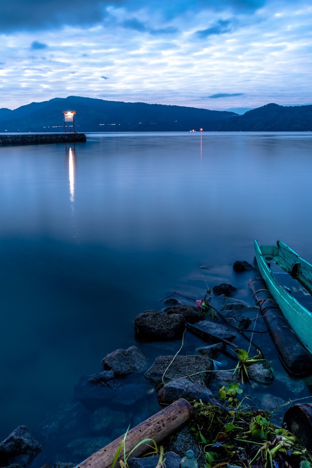 Деревянная лодка на берегу тихого озера в сумерках 