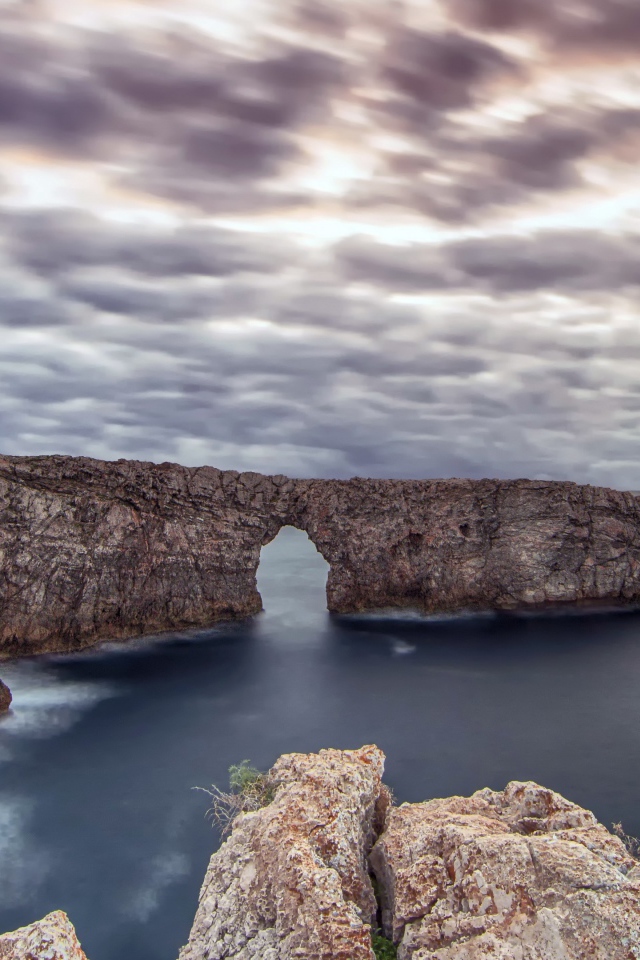 Арка в скале в море под пасмурным небом 