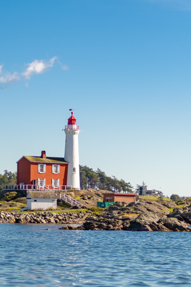 Маяк на каменном берегу моря под голубым небом 