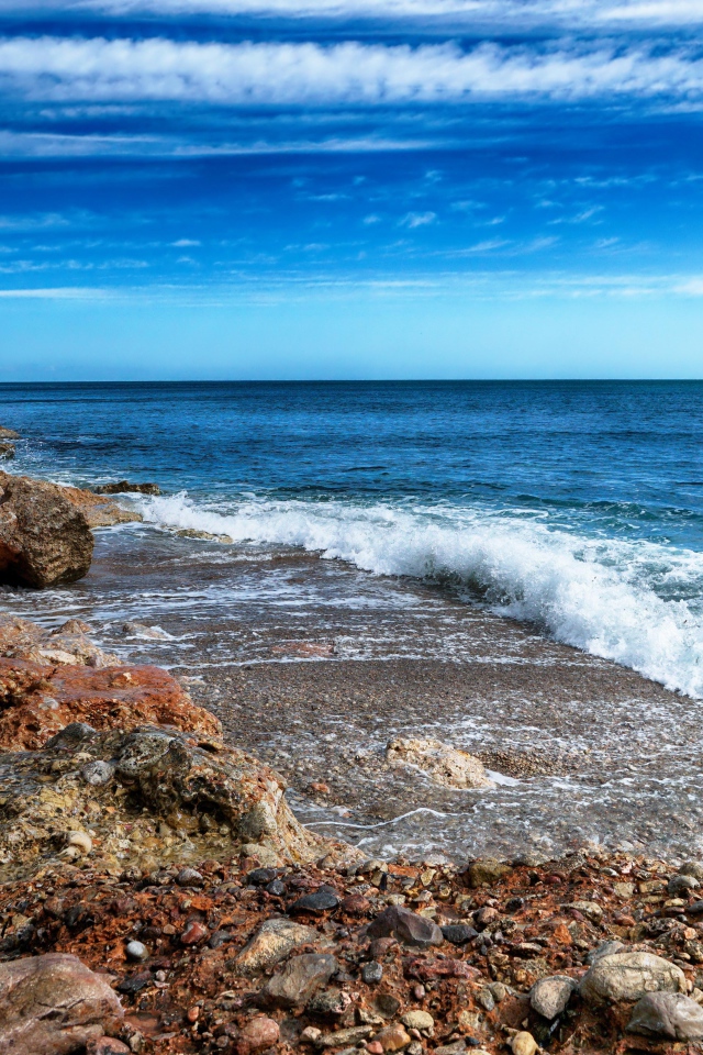 Белые волны на берегу моря с большими камнями под голубым небом