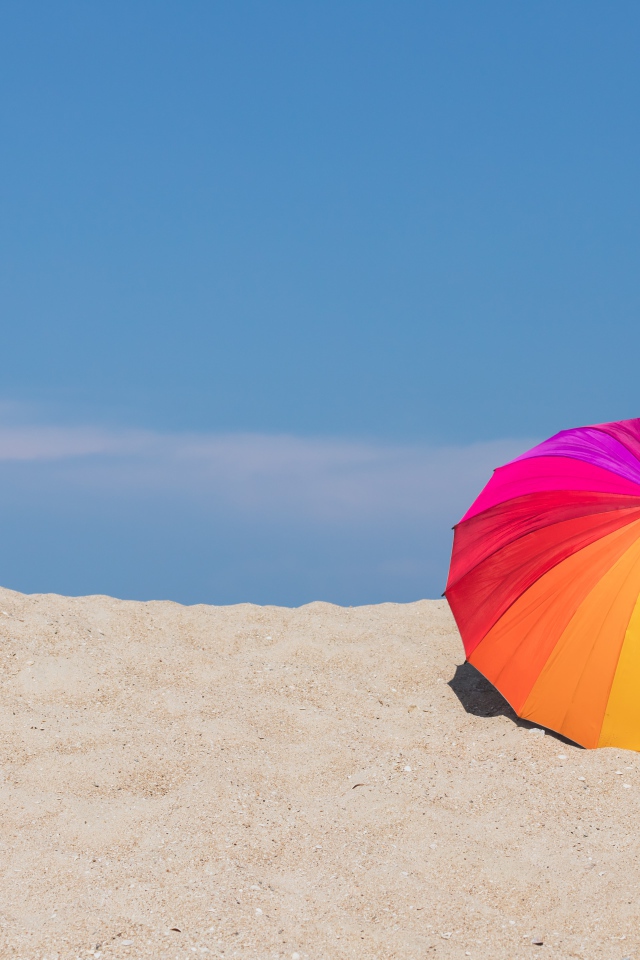 Разноцветный зонт лежит на горячем песке летом