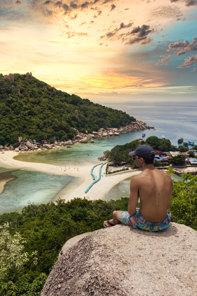 Мужчина сидит на краю скалы на закате 