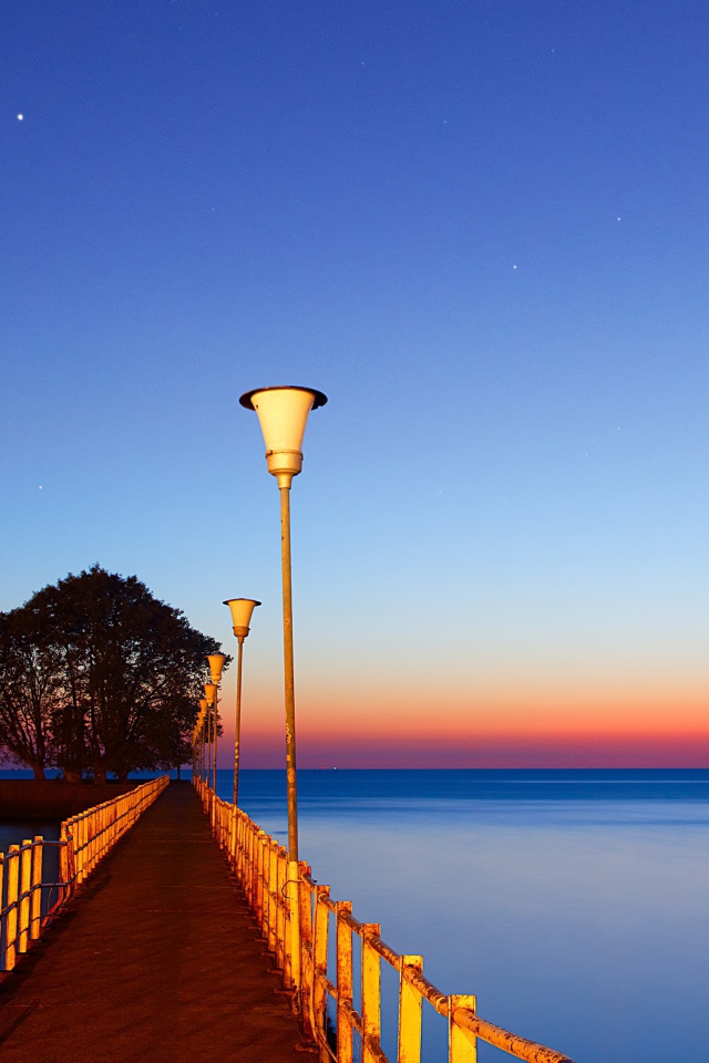 Мост в фонарями в море на закате 