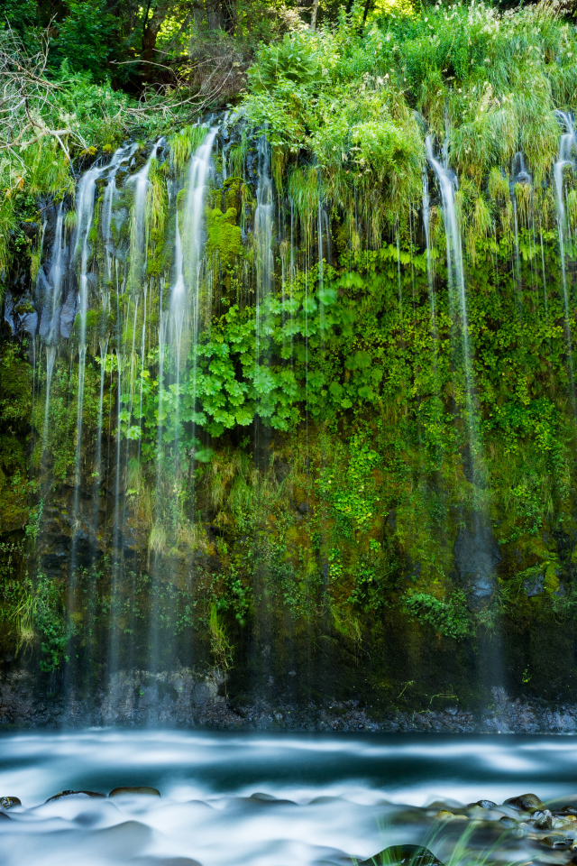 Красивый водопад стекает по покрытом зеленью утесе 