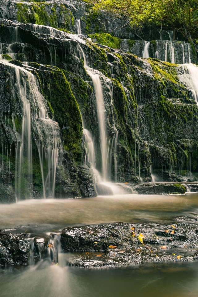 Водопад в лесу стекает по покрытым мхом камням 