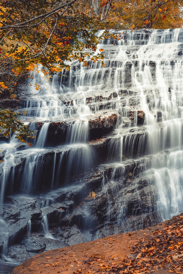 Быстрая вода водопада стекает по каскадам камней осенью