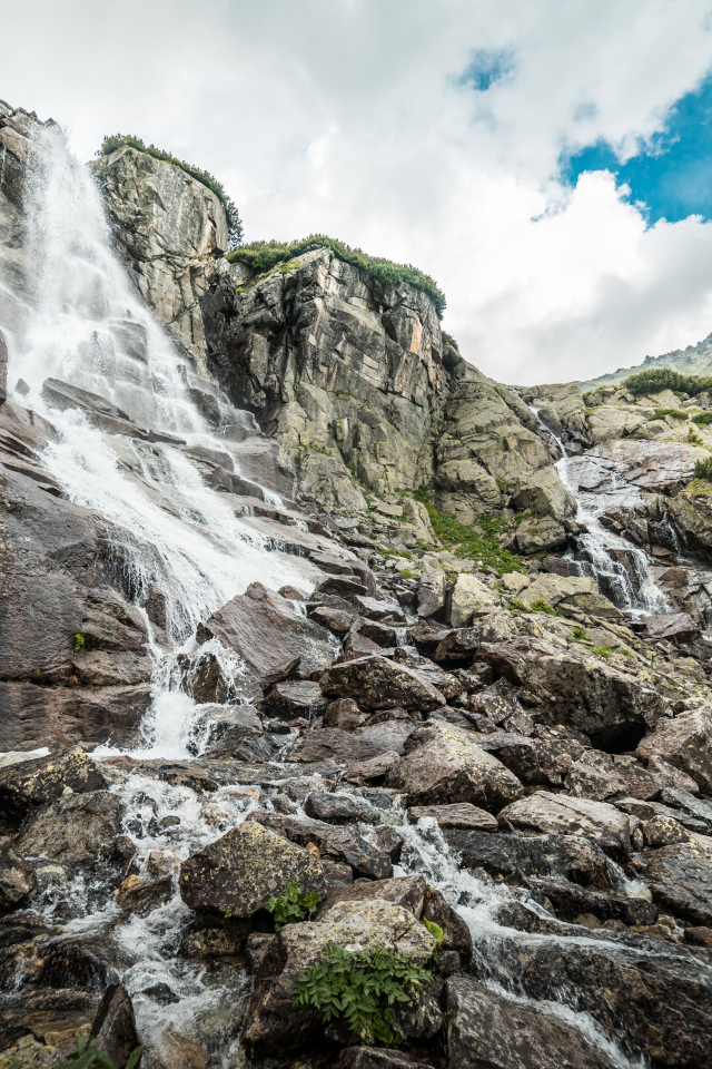 Водопад стекает по камням на фоне неба с белыми облаками