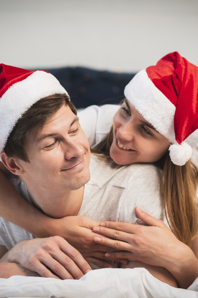 A man and a girl in Santa Claus hats lie on the bed
