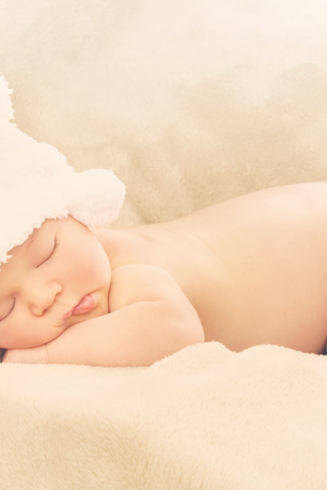 Грудной ребенок с белой шапке спит на кровати