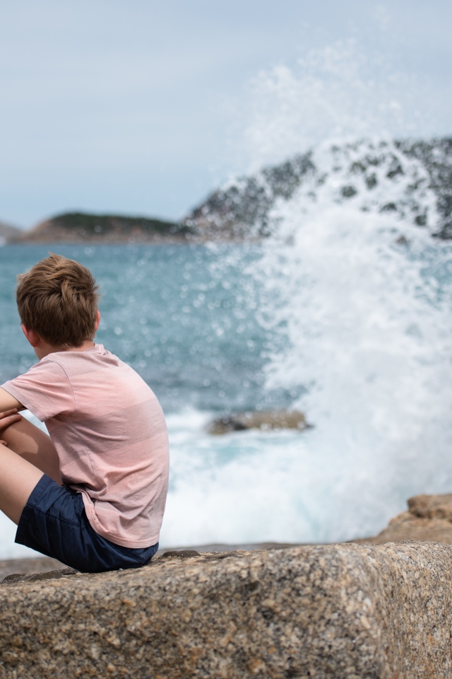Мальчик сидит на камнях у бушующего моря