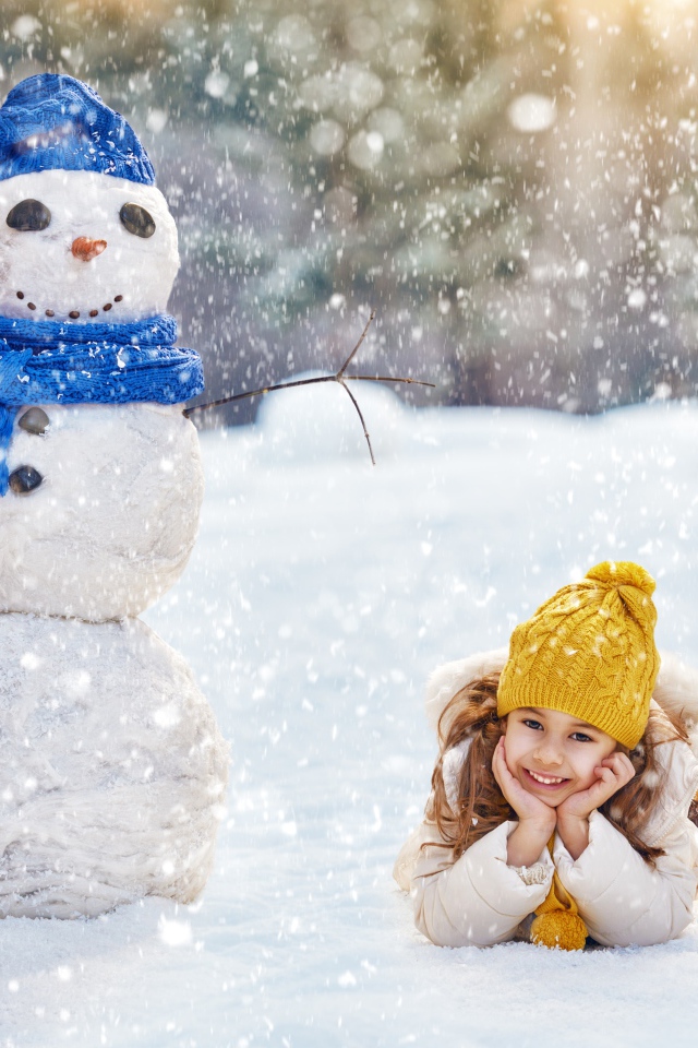 Милая девочка лежит на снегу у снеговика зимой