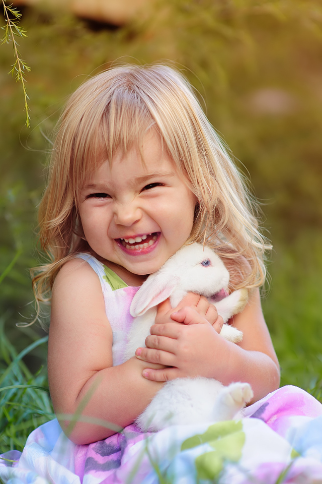 Довольная маленькая девочка обнимает белого кролика на траве 