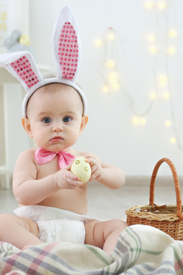 Милый ребенок с ушками на голове сидит пасхальными яйцами