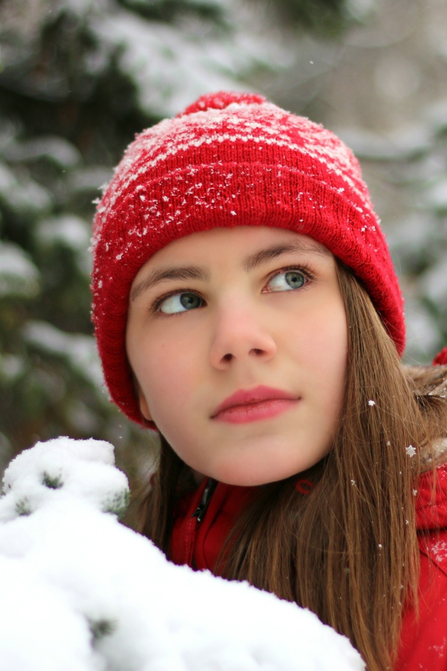 Милая девочка в красной шапке у заснеженной ели