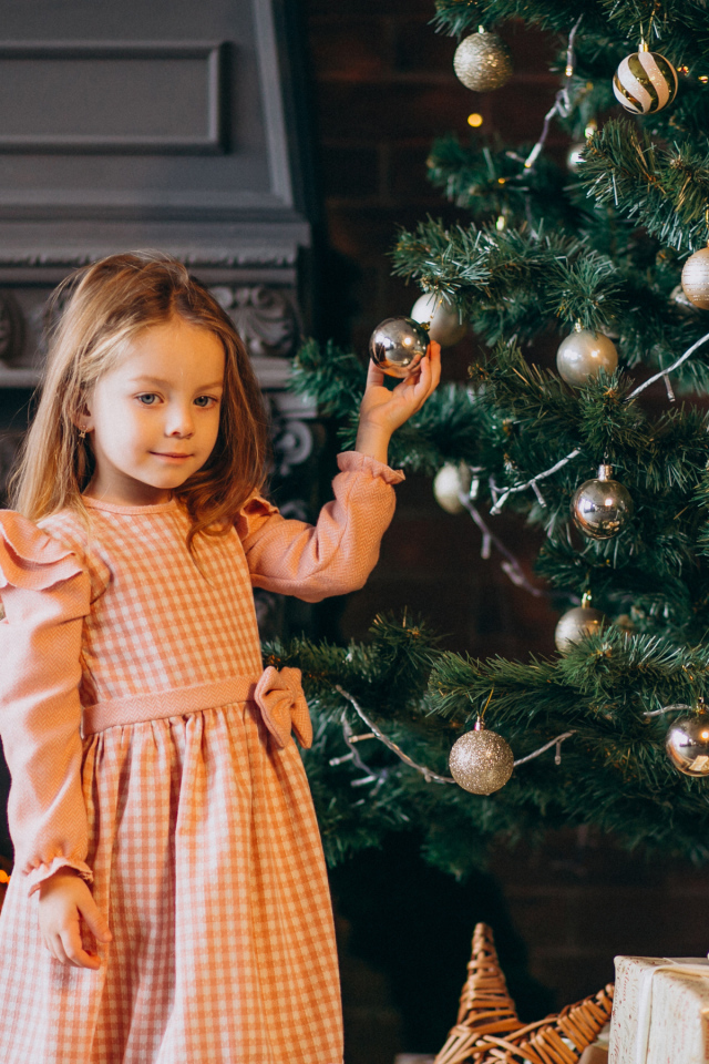 Милая маленькая девочка стоит у наряженной елки 