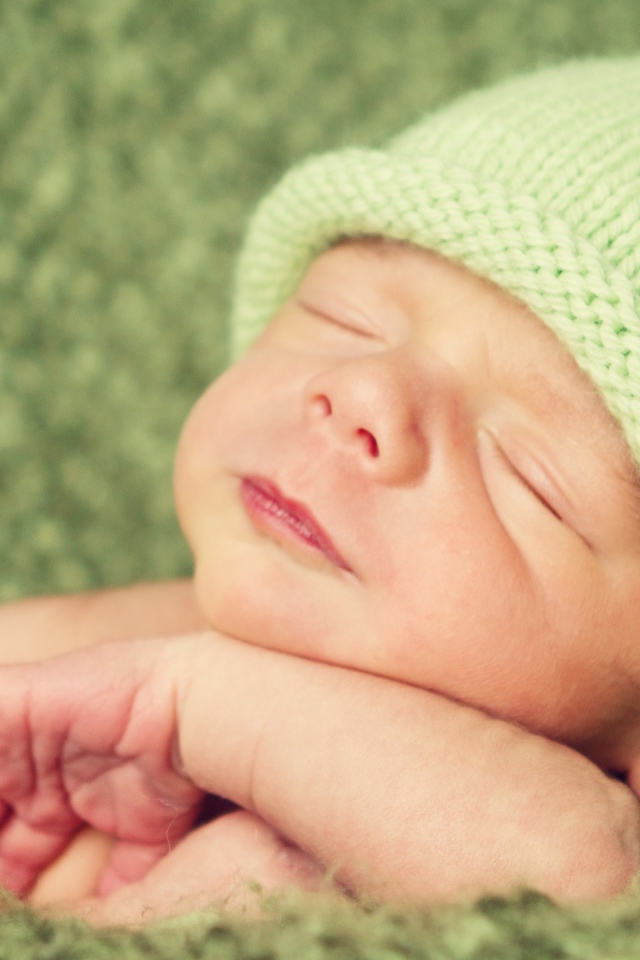 Зеленая вязаная шапка на голове у спящего ребенка 