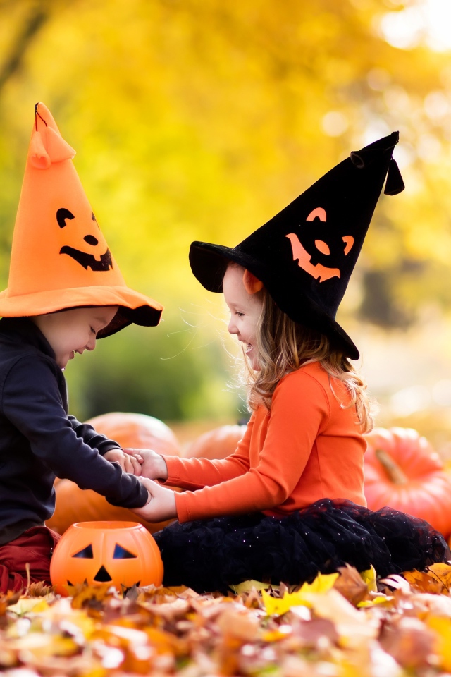 Маленькие мальчик и девочка в костюмах на Хэллоуин сидят на листве