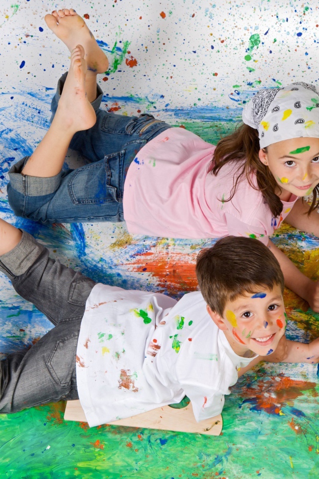 Маленькие мальчик и девочка рисуют красками на полу 