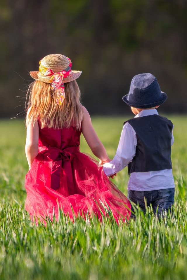 Маленькие мальчик и девочка идут по зеленому полю