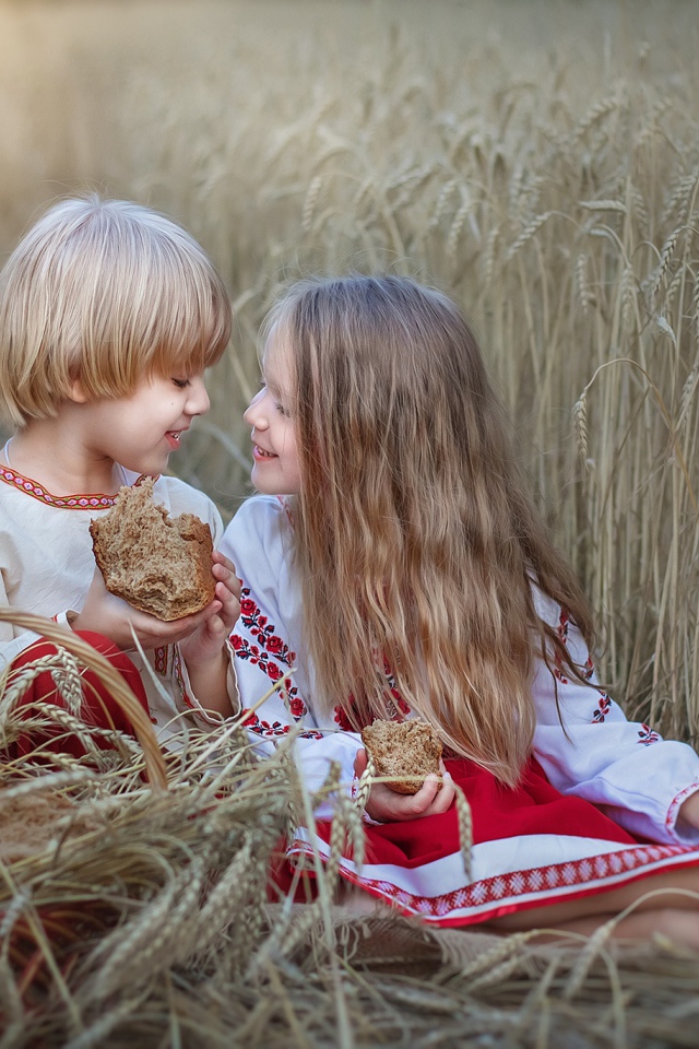 Маленькие мальчик и девочка с хлебом на пшеничном поле 