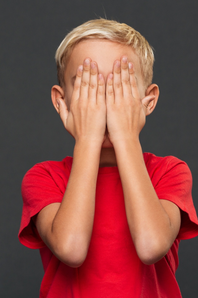 Маленький мальчик в красной футболке закрыл лицо руками 
