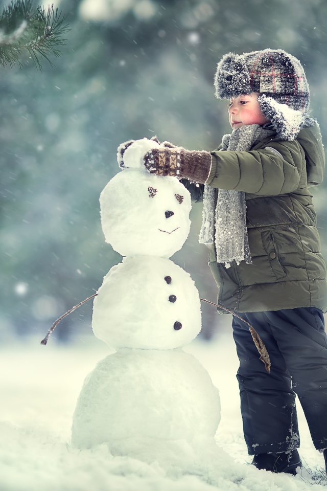 Маленький мальчик лепит снеговика зимой