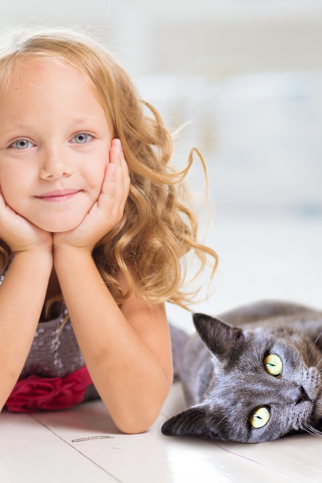 Маленькая милая голубоглазая девочка лежит на полу с котом