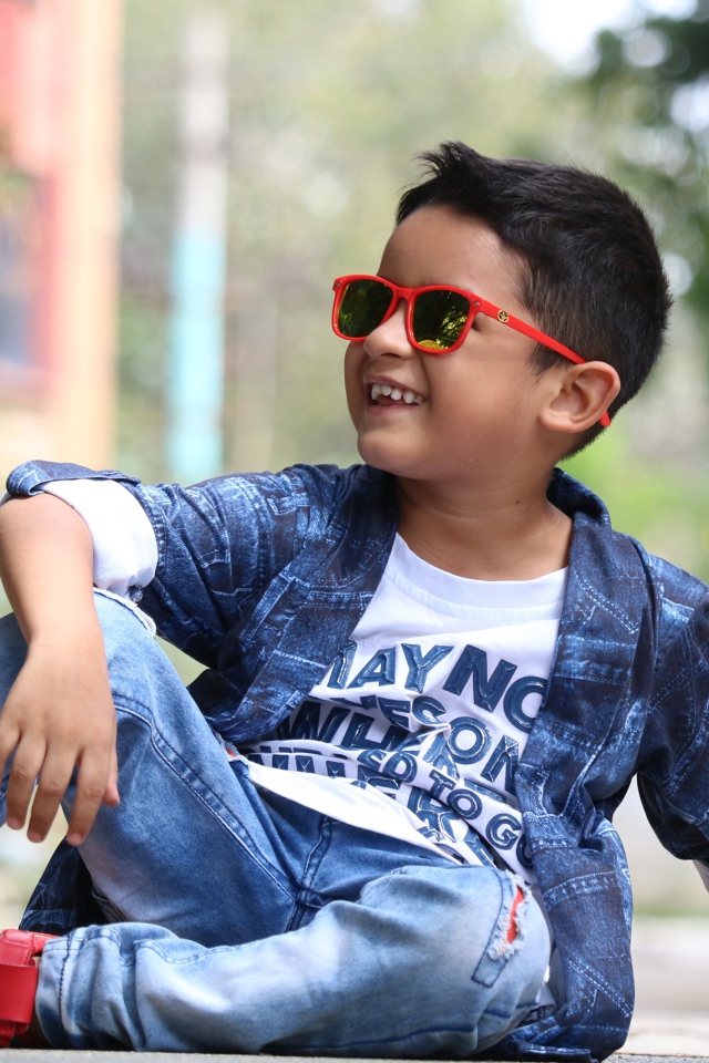 Маленький модный мальчик сидит на асфальте