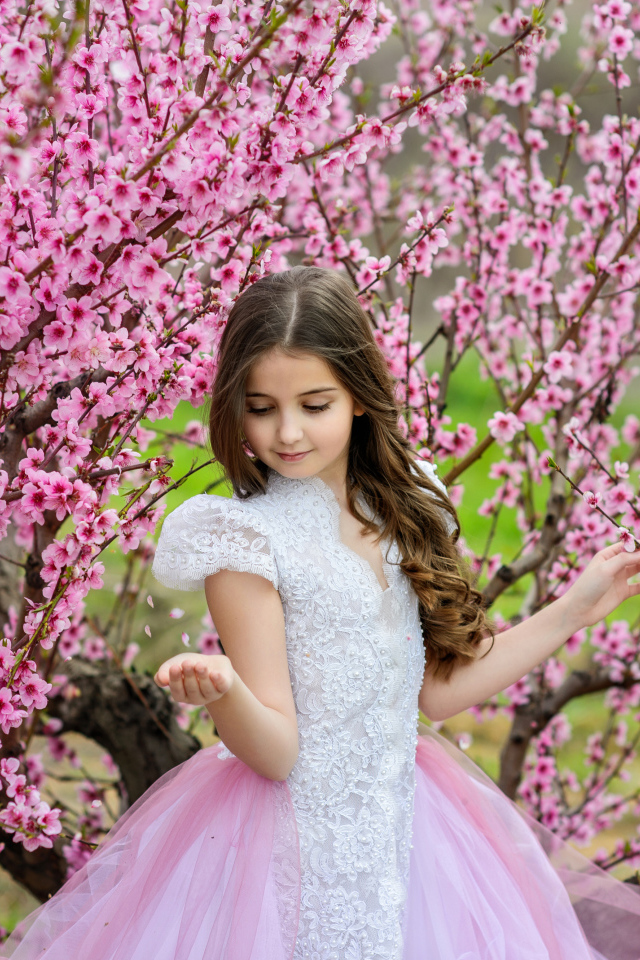 Маленькая девочка в красивом платье у дерева с розовыми цветами