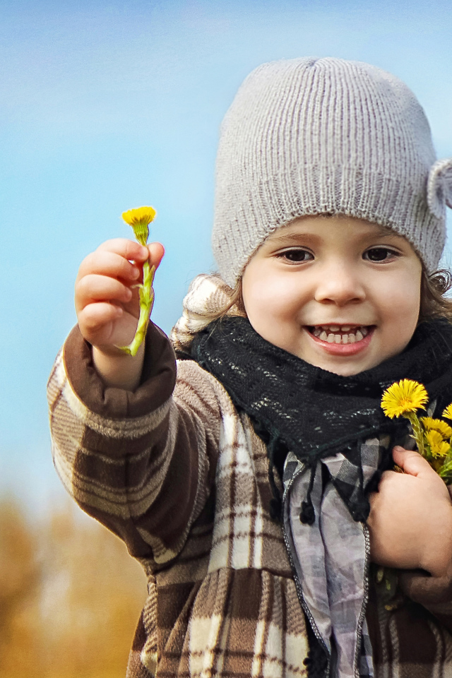 Маленькая девочка в шапке с желтыми цветами в руке