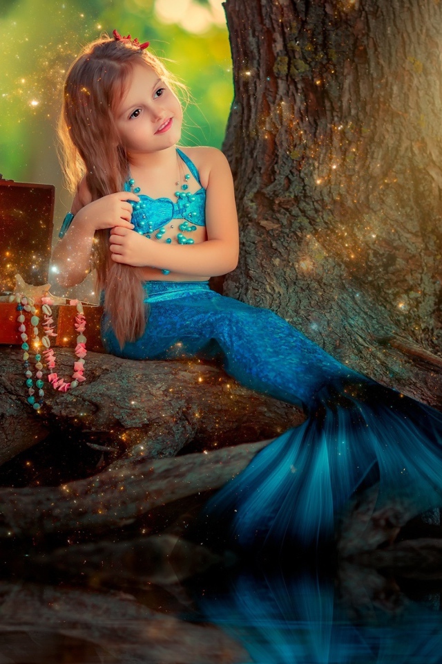 Маленькая девочка в костюме русалочки сидит у воды 