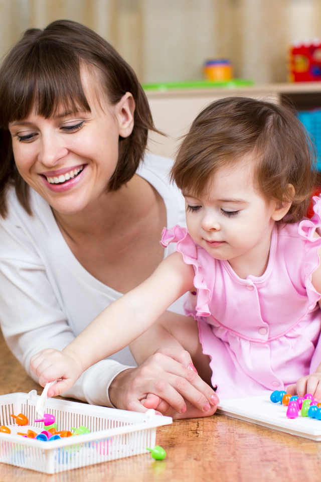 Маленькая девочка в розовом платье играет с мамой