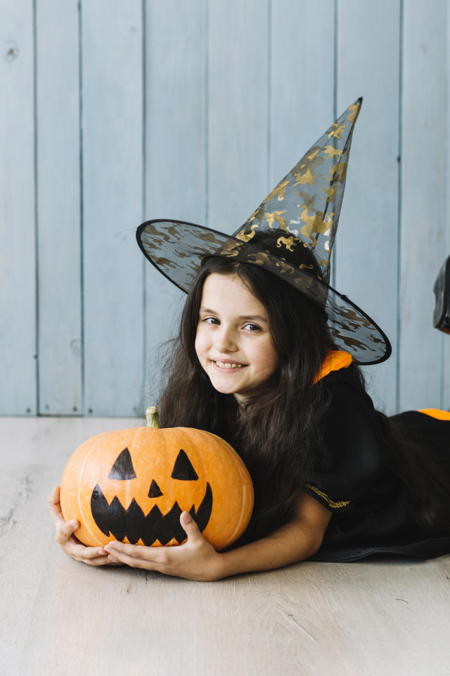 Маленькая девочка в костюме ведьмы с тыквой на Хэллоуин