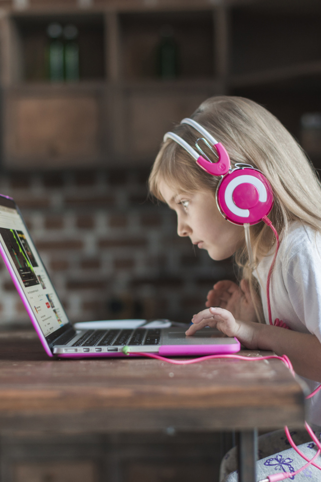 Маленькая девочка в наушниках сидит за ноутбуком