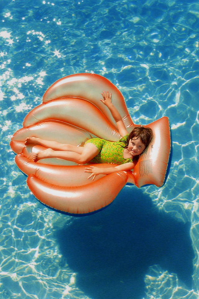 Маленькая девочка на надувном матрасе в бассейне летом 