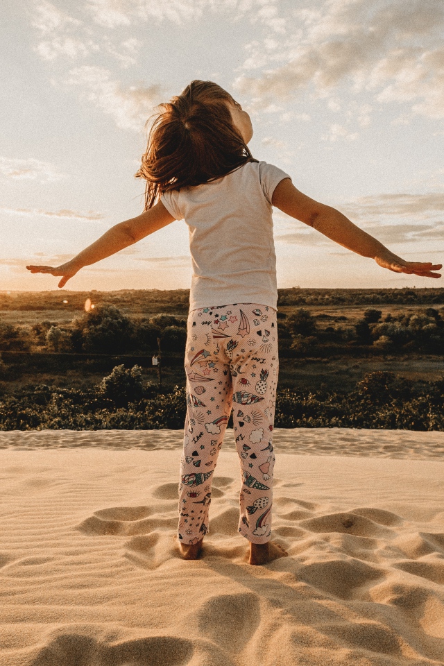 Маленькая девочка стоит на песку в лучах солнца