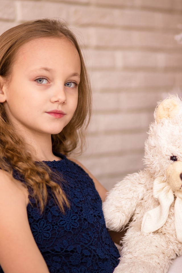 Маленькая девочка с мишкой сидит у наряженной ели 