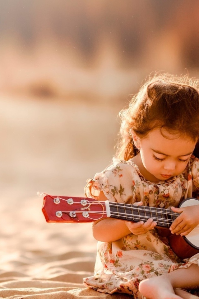 Маленькая девочка с гитарой сидит на песке 