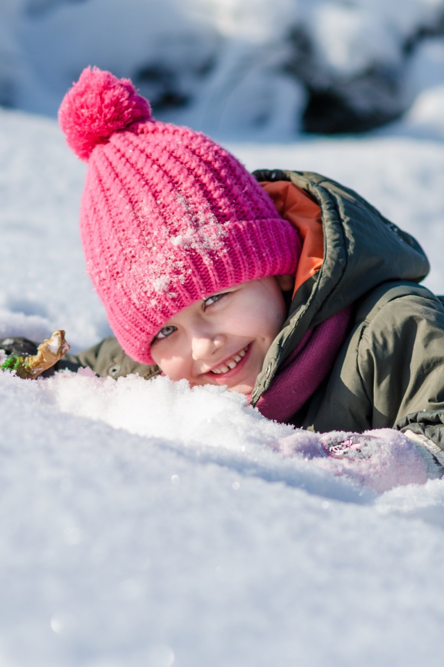 Маленькая улыбающаяся девочка лежит на снегу