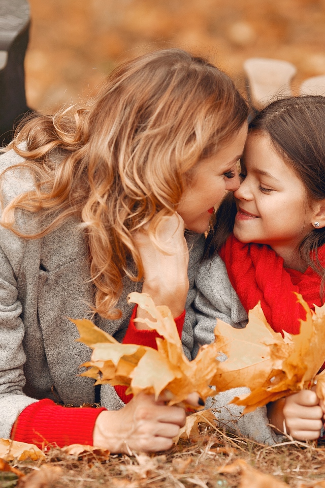 Мама с дочкой лежат на листве осенью 