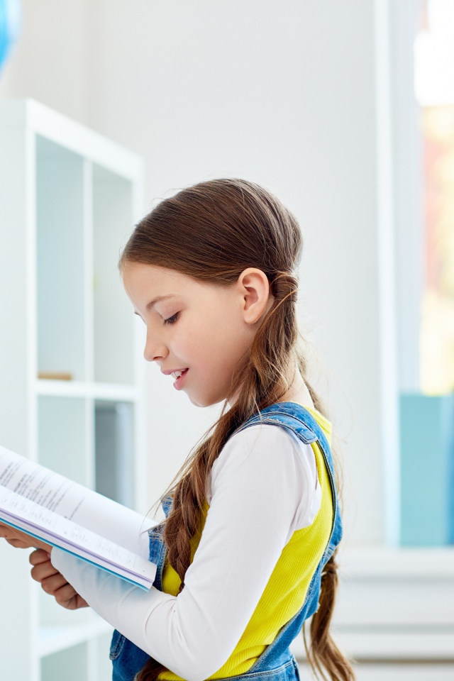 Умная девочка школьница с книгой в библиотеке 