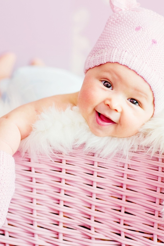 Улыбающийся грудной ребенок в шапке в розовой корзине 