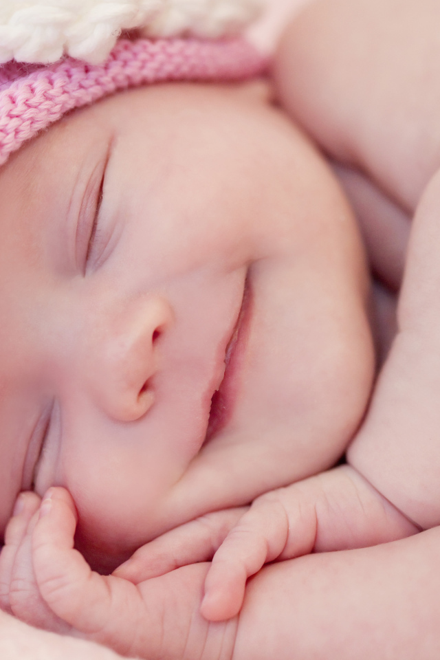 Улыбающийся грудной ребенок в розовой вязаной шапке 