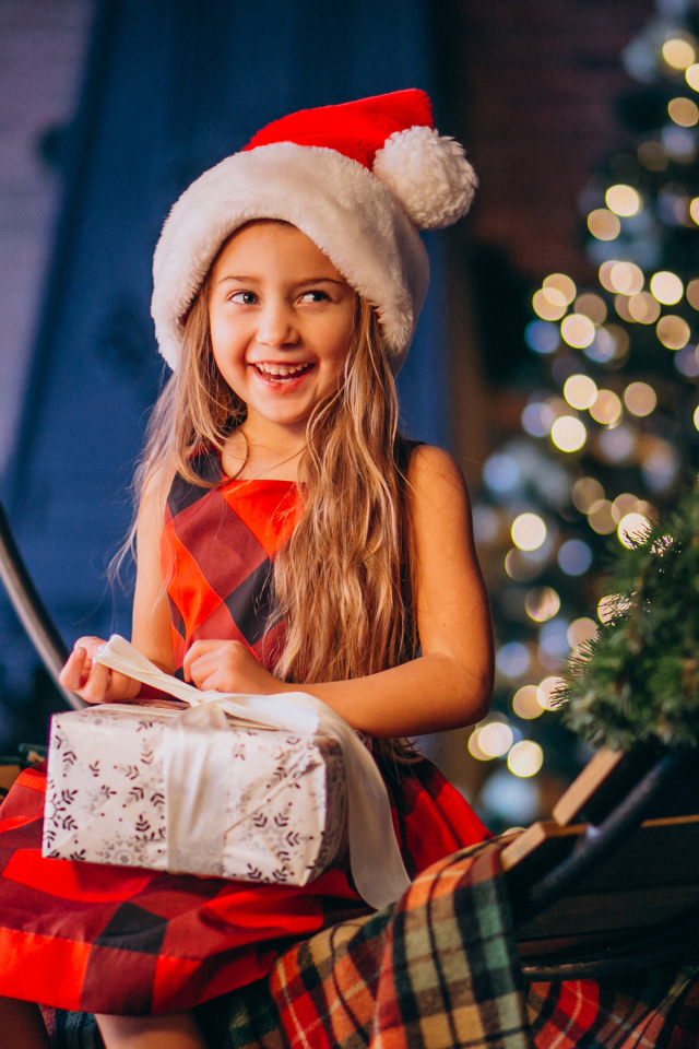 Улыбающаяся девочка сидит с подарком на Рождество 