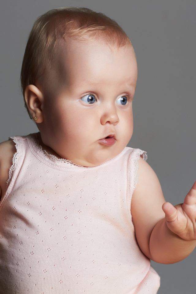 Удивленный маленький ребенок на сером фоне