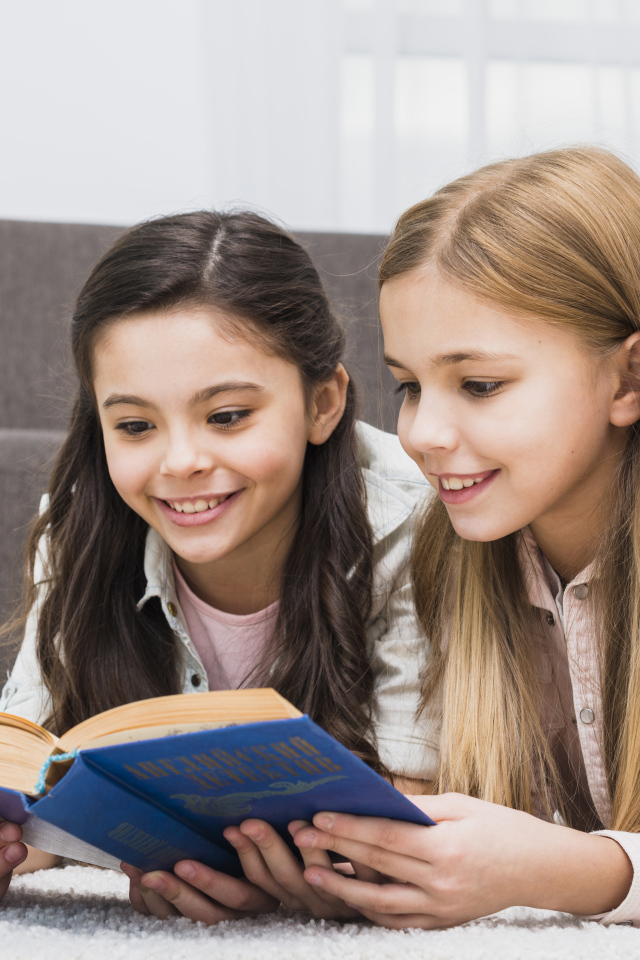 Две маленькие девочки читают книгу на полу