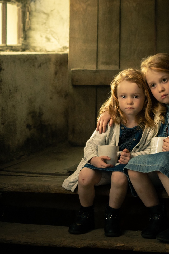 Две маленькие сестры пьют какао на ступеньках дома