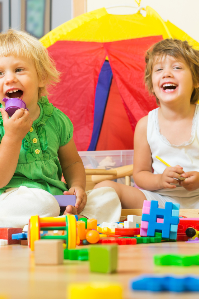 Два улыбающихся ребенка играют с конструктором 